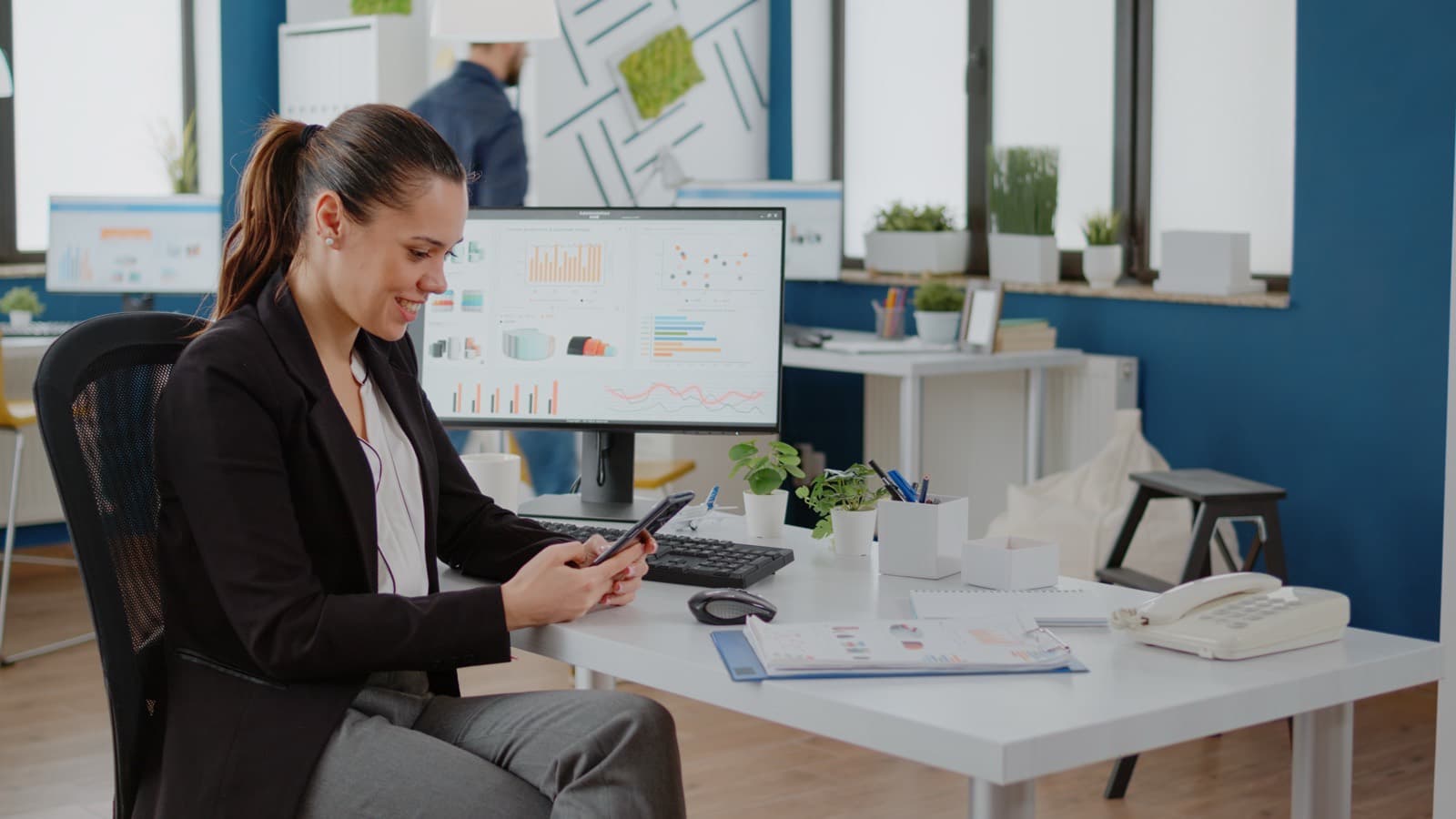 Business professional reviewing charts on a computer while using a smartphone for planning