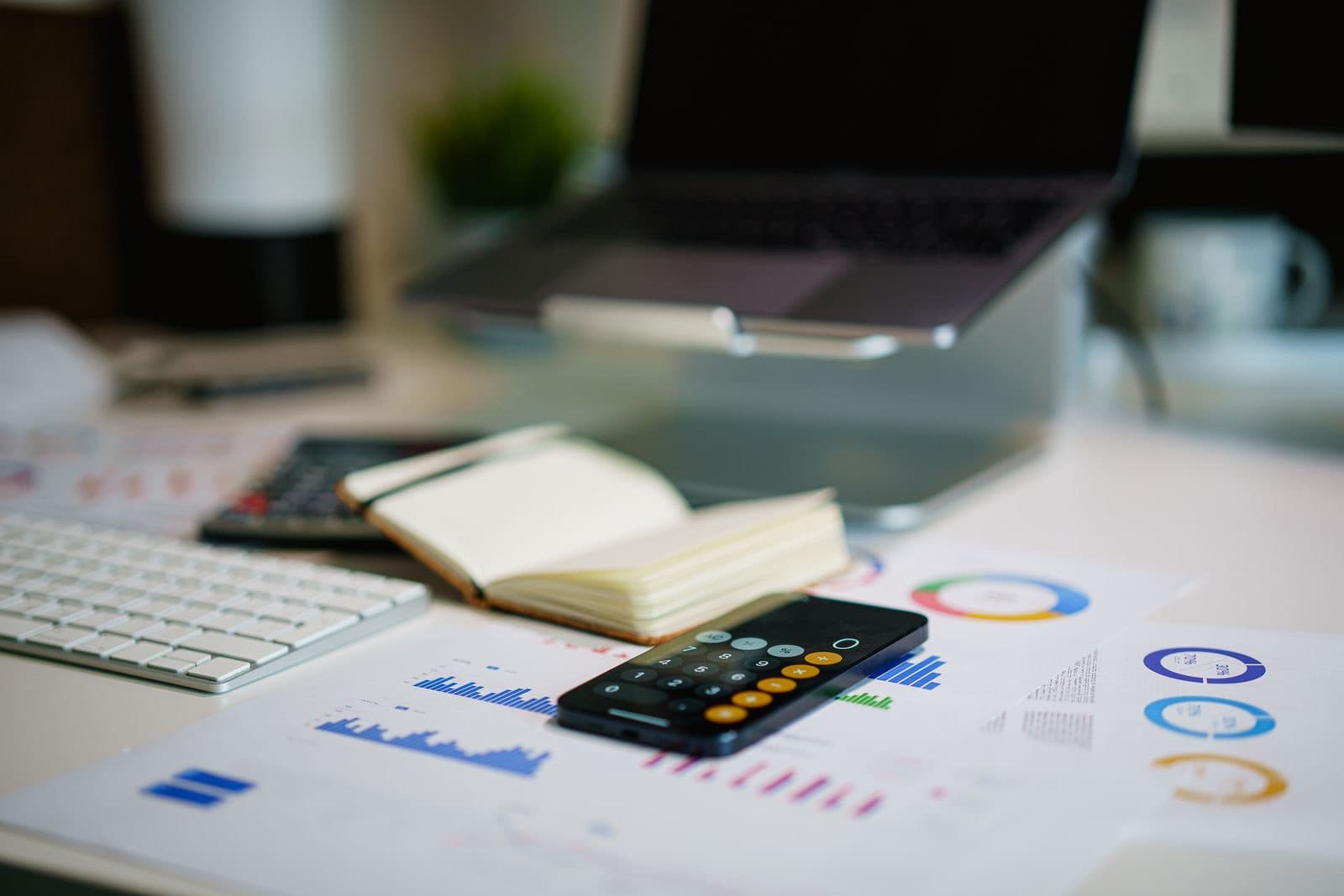 Smartphone calculator on a desk with financial charts and a laptop